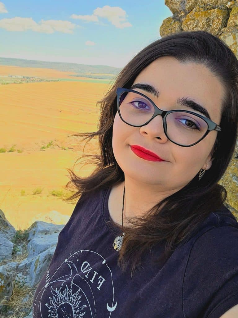 Peaceful woman with spiritual necklace overlooking fields and sky, cultivating inner peace and enlightenment.